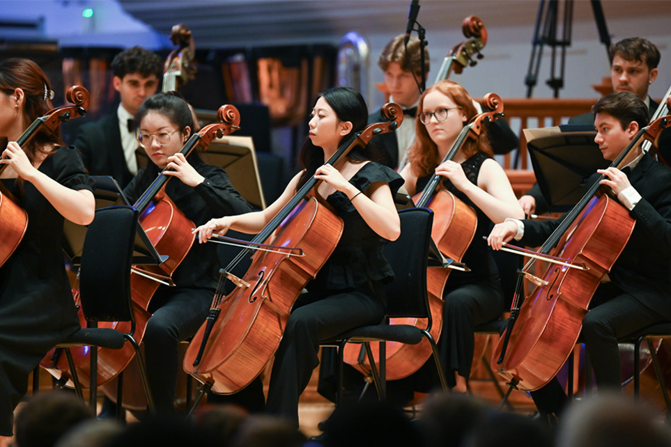 A group of musicians, wearing smart black attire, playing the cello in an orchestra.